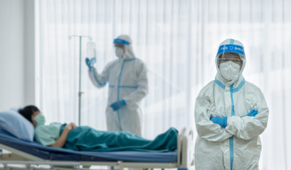 two doctor in personal pretective equipment or ppe treating the asian woman patient with covid-19 or coronavirus infection in the isolation unit in the hospital during pandemic. medical concept