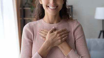 Close up focus on happy sincere female holding folded hands on chest. Emotional positive kind...