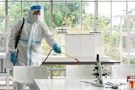 Worker From Decontamination Services Wearing Personal Protective Equipment Or Ppe Including Suit, Face Shield And Mask. He Uses Disinfectant To Spray And Clean Scientist Lab