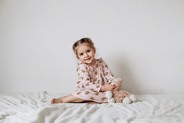 Little three year old girl plays and hugs a toy cat on a white background