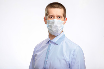 A serious man in a medical mask, a light shirt looks into the camera. Isolated