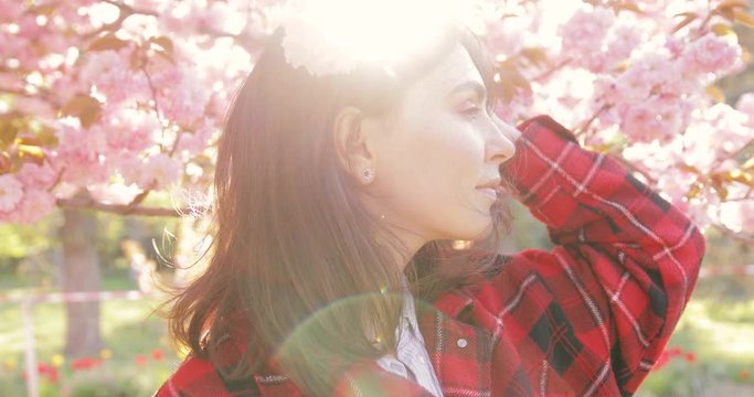 Beautiful young woman meditating near tree against pink cherry blossom trees, enjoy the wind blowing her face and hair with eyes closed, 4k footage, slow motion.