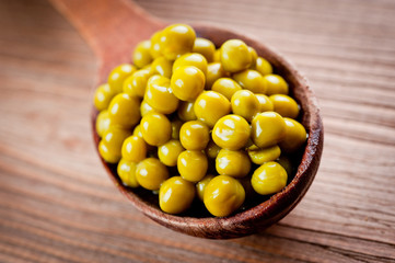 Canned green peas in a wooden spoon lying on a wooden surface of the table.