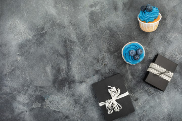 Blueberry muffins with blue cream and gifts on dark background. Flat lay