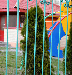 Fototapeta na wymiar Metal fence on the background of a green tree and a Playground.