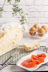 Half of Round loaf of freshly backed homemade white bread and pieces of salted salmon on white plate. Hight key.