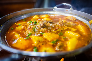 Spicy yak meat in hotpot and fried pig in white plate on wooden table