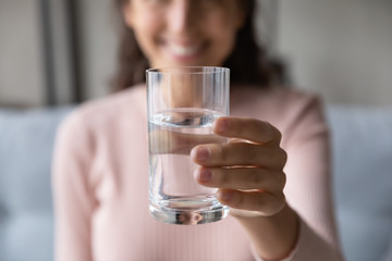 Close up happy woman pulling out hand with glass of fresh cool water. Smiling lady recommending drinking pure distilled aqua every day, preventing organism from dehydration, healthcare concept.
