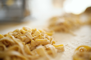 Staying at home with your family and preparing fresh home-made pasta (tagliatelle): mom creating nests of pasta noodles on a wooden board.