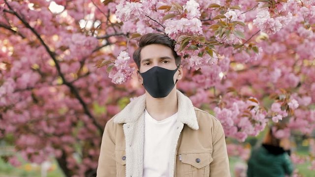 Portrait of stylish hipster man looking in camera and wear black protective mask. Fresh air, no pollution, clear sky and nature concept. Save the planet