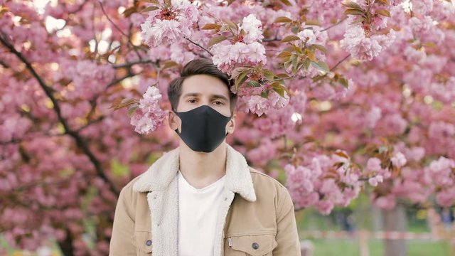 Portrait of Young Handsome Man Wearing Black Medicine Mask Inhaling and Exhaling Fresh Air, Taking Deep Breath, Looking into the Camera. He is Smiling. Healthy Lifestyle Concept.