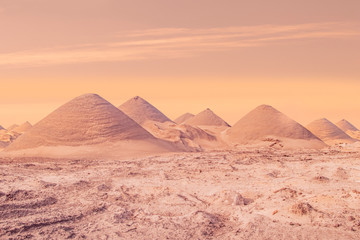 Fototapeta na wymiar A beautiful warm and pinkish background travel image of many sandy dunes, pyramids or hills under a cloudy sunset and some sandstorm dust in asia or africa with copy space