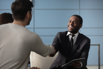 Handsome african american businessman in suit shaking hands with man in office. Happy smiling...