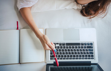 Asian woman is using a notebook computer for work at home and she is sitting on her bed and she is quarantine during the coronavirus epidemic.