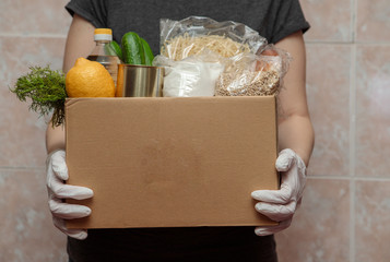 Food delivery. Food in a box, in hands with gloves, close-up. Coronavirus volunteer, food donation.