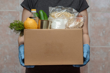 Food delivery. Food in a box, in hands with gloves, close-up. Coronavirus volunteer, food donation. - 343010709