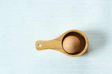 Single raw fresh chicken egg or boiled egg in wooden spoon on isolated white gray line texture background