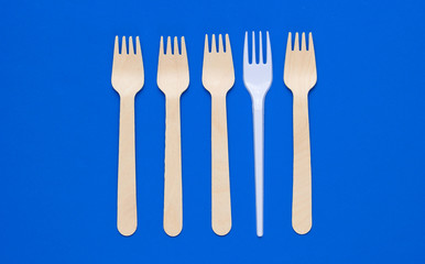 Minimalistic environmental concept. Wooden and plastic forks on blue background. Creative eco background. Top view