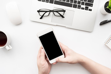 Man is using smartphone with blank screen over white office desk table with laptop computer and supplies. Top view.