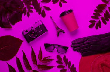 Jorney to Paris. Women's accessories (hat, gloves, sunglasses), retro camera, figurine of the Eiffel tower in pink neon light with green leaves. Top view