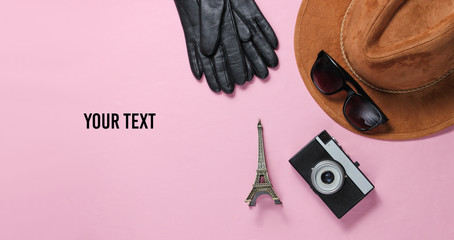 Jorney to Paris. Women's accessories (hat, gloves, sunglasses), retro camera, figurine of the Eiffel tower on pink background. Top view. Copy space