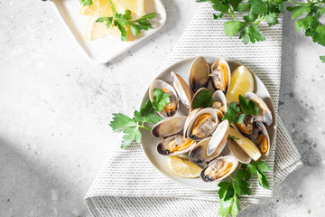 Cooked clams in a ceramic plate on a light gray table. Seafood dish. The view from the top