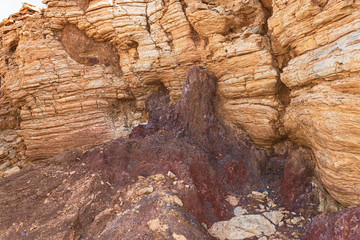 detail of the wall of an abandoned quarry called the cave in the makhtesh ramon crater in israel showing colored soild, sand, and limestone layers and desposits of clay