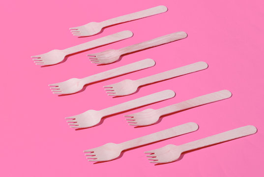 Many eco-friendly wooden forks on pink background. Minimalistic eco concept. Pop art
