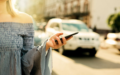 Online taxi call. Young attractive woman orders a taxi using a mobile app on a busy roadway of the city