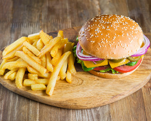 Fresh delicious burger , bacon, cheese, tomato, french fries onion and lettuce on wooden table