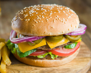 Fresh delicious burger , bacon, cheese, tomato, french fries onion and lettuce on wooden table