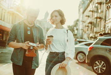 Young couple of hipster tourist with a retro camera are talking to each other while walking around the city. Romantic love story