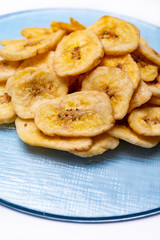 Healthy snack, crispy dehydrated unsugared banana chips on recycled glass plate on white background