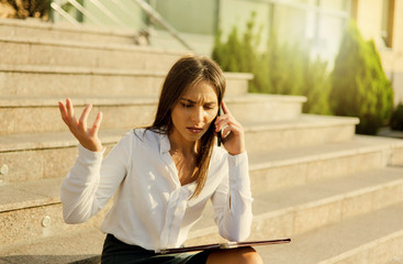 Emotional upset business woman talking on the phone while sitting on the stairs outdoors