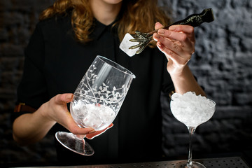 female bartender neatly puts piece of ice with tongs in glass