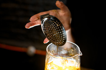Close-up. Steel strainer in girl's hand on glassy mixing cup.