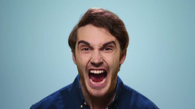 Angry man screaming in studio. Rage guy shouting on blue background