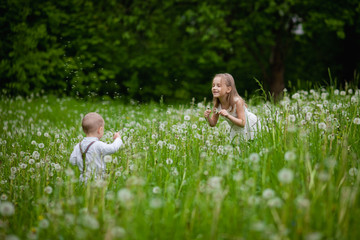 A girl blows on a dandelion. A little boy and a girl have fun on the street. Brother and sister play in the street. Spring, the concept of allergies to pollen, selective focus, close-up.