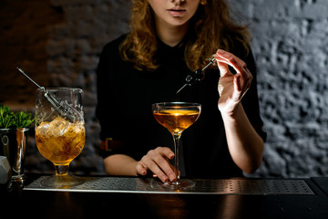 girl at bar holds small sword with cherries over glass with cocktail