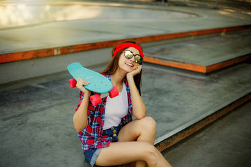 Portrait of stylish skater woman in skatepark. Attractive girl in red plaid shirt, mirrored sunglasses, shorts rests with a skate © splitov27