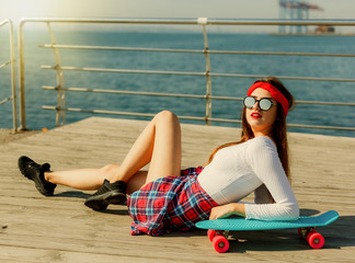 Portrait of stylish skater woman at beach. Attractive sexy woman lies on skate outdoor