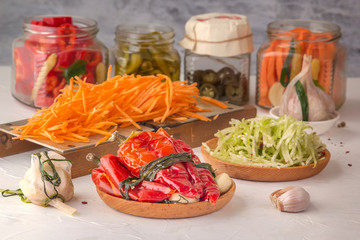 Fermented red hot peppers to enhance immunity with spices and grated carrots on a hand grater on a light wooden table against a background of glass jars with pickled products