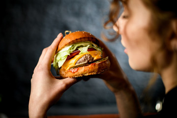 Close-up of hamburger in hands of young woman. - obrazy, fototapety, plakaty