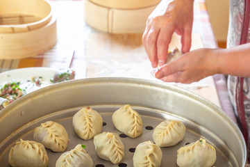 Female hands make manti, khinkali, dumplings or wonton from dough with minced meat filling and greens on the background of the kitchen table with a double boiler. Homemade food.