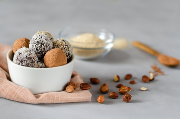 Vegan energy balls in a bowl with hazelnuts on a gray background. Natural sweets from nuts and dried fruits in coconut, cocoa and sesame seeds, close-up. The concept of raw food sweets without sugar