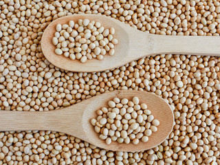 Soya in a wooden spoon, top view on a background of scattered soybeans. Vegan. Natural food. Suitable for background.
