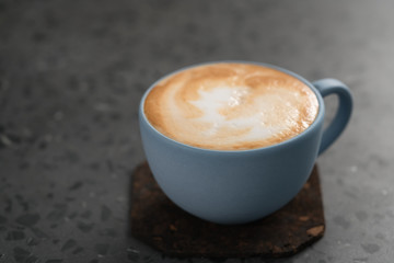 Fresh cappuccino in blue cup on concrete background