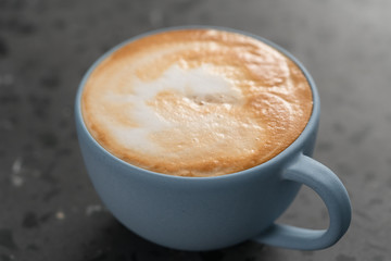 Fresh cappuccino in blue cup on concrete background