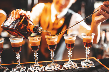 The bartender makes cocktails with liquor, using a bar spoon. layered cocktails. Bar counter. Atmospheric photo with warm tinting