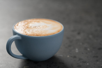 Fresh cappuccino in blue cup on concrete background